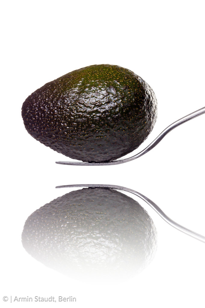 an avocado laying on a fork with reflection, isolated on white