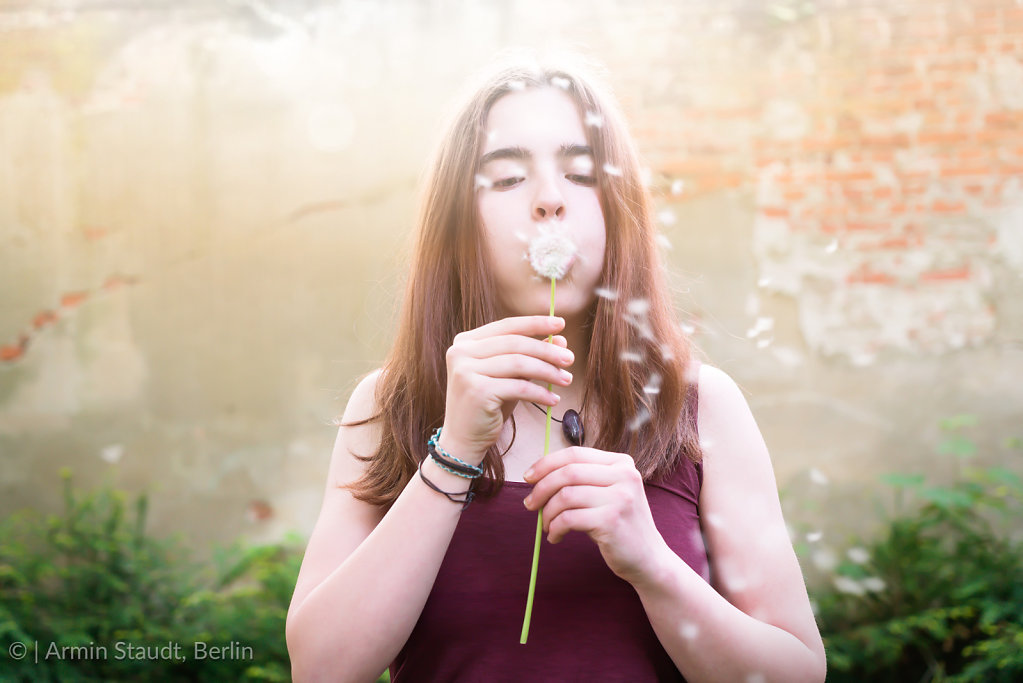 Pretty girl blowing dandelion in front of an old wall